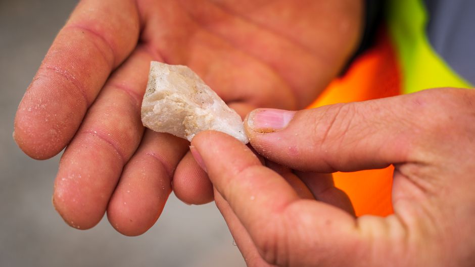 Detailed close-up of hands examining a white mineral stone outdoors.